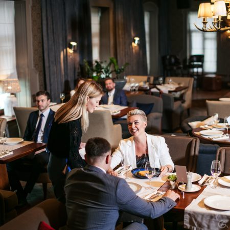 In modern restaurant couple of young people talks to pleasant waitress, cheerful woman smiles broadly, thanks kind female for good service, right side shot